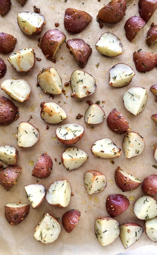 A sheet pan full of sliced and roasted baby red potatoes with herbs. 