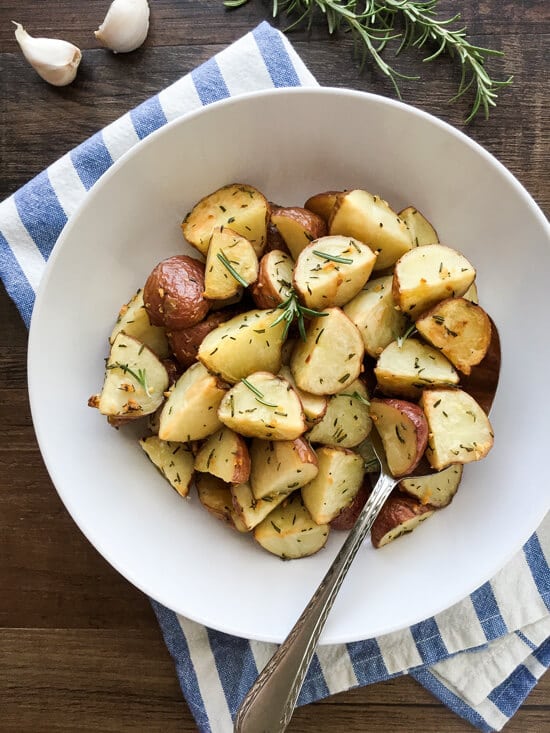A bowl of sliced and roasted baby red potatoes with herbs. 