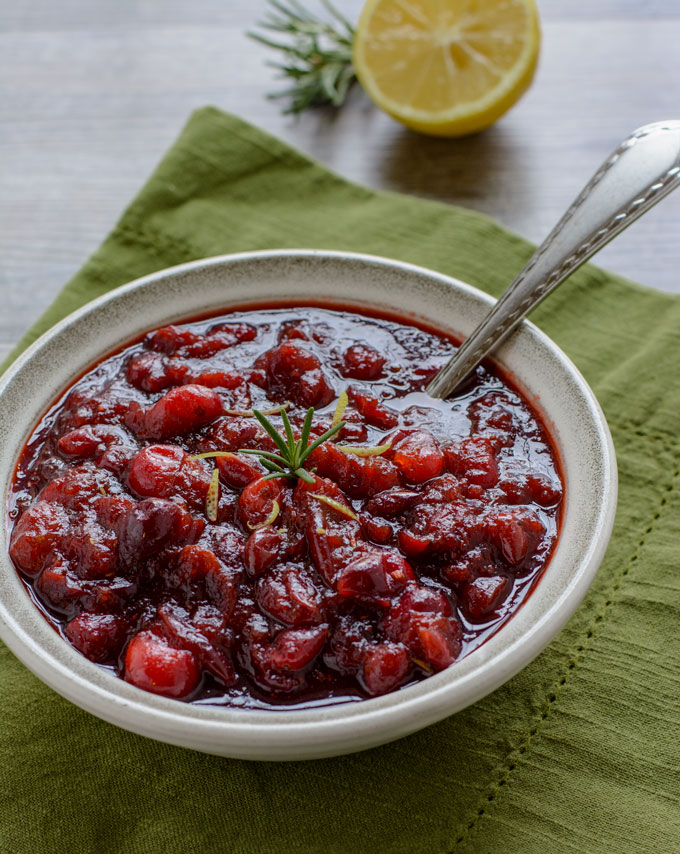 A bowl of cranberry sauce topped with a sprig of rosemary and some lemon zest. 