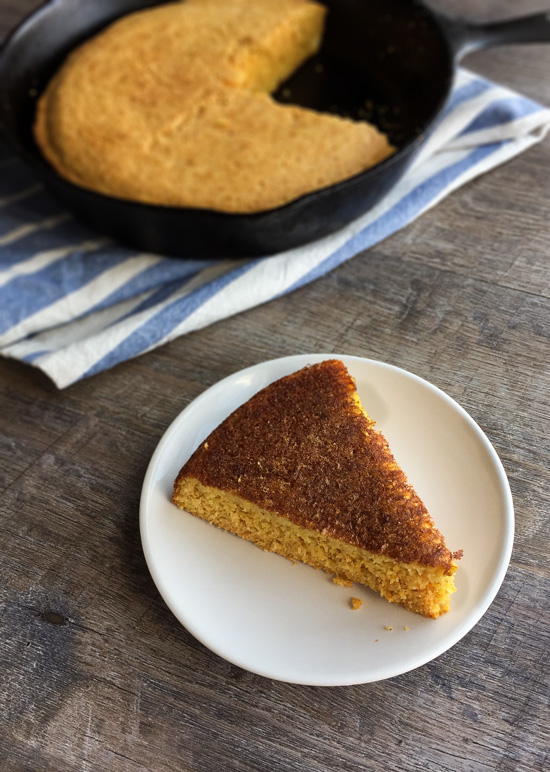 A cast iron skillet of cornbread with one piece cut out and placed onto a plate.