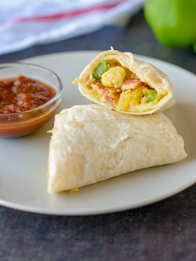 A small plate with a bowl of salsa and a cut in half breakfast burrito sitting on it. 