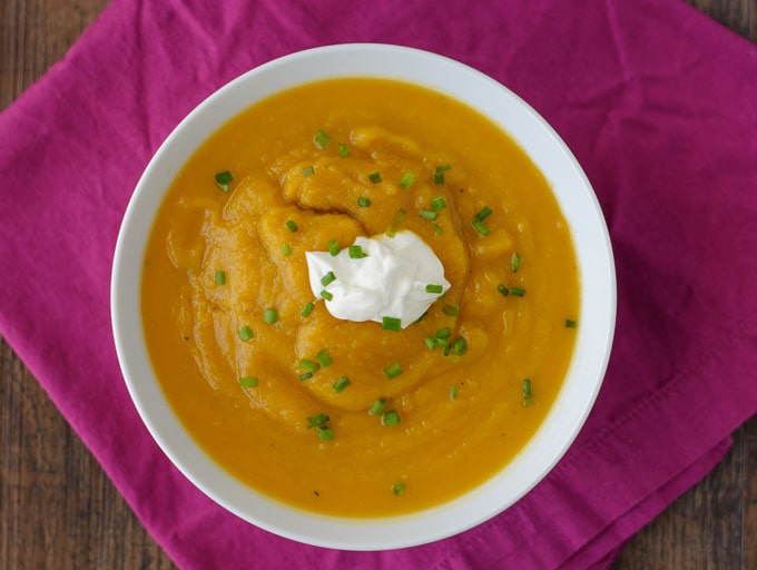 Overhead picture of a bowl of butternut squash soup topped with sour cream and chives. 