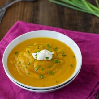 A bowl of butternut squash soup topped with sour cream and chives.