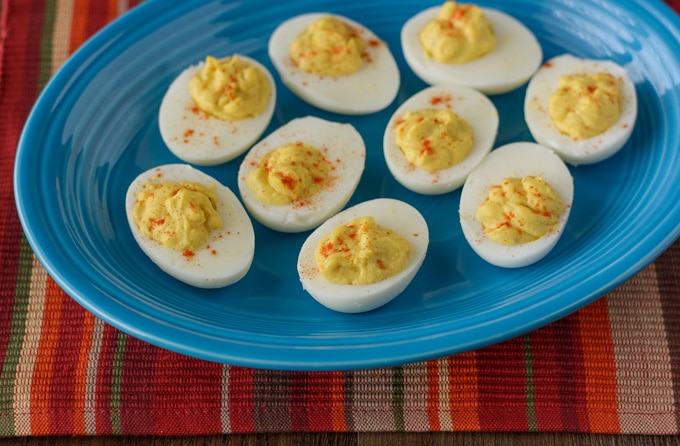 Deviled Eggs topped with a sprinkle of paprika sitting on a blue platter.