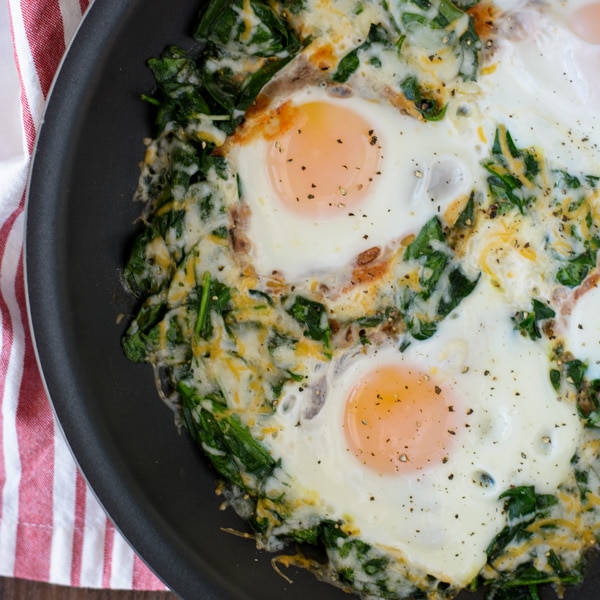 A non-stick skillet with wilted spinach, cheese and cooked eggs.