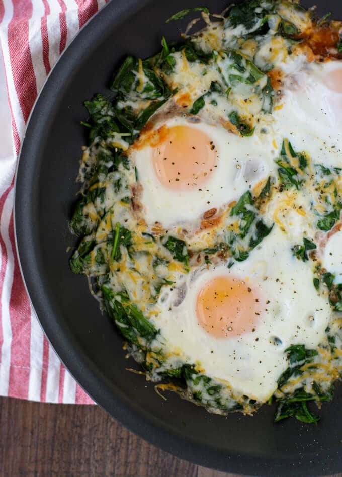 A skillet with wilted spinach, eggs and melty cheese.