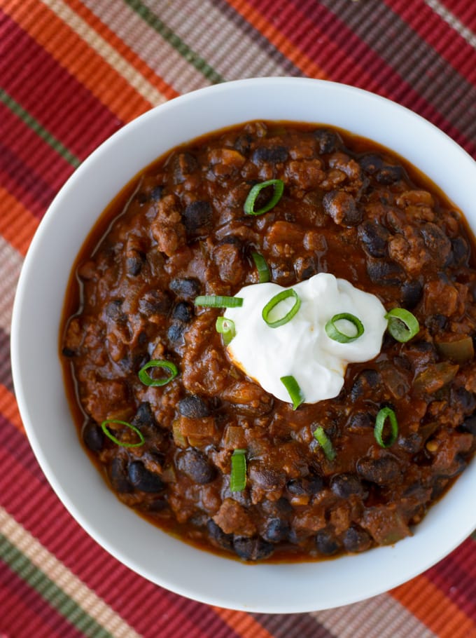 A bowl of Chili con Carne topped with sour cream and green onions sitting on a placemat. 