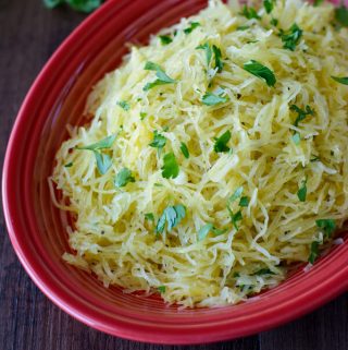 A red platter filled with cooked spaghetti squash topped with parsley.
