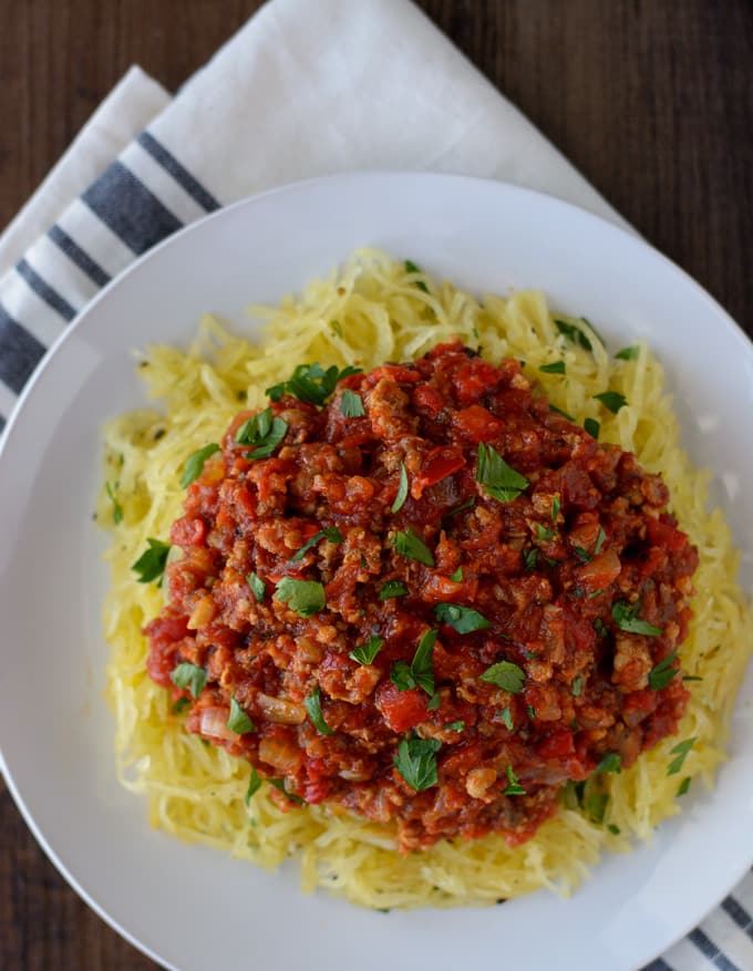 A white plate with shredded spaghetti squash topped with Italian meat sauce.