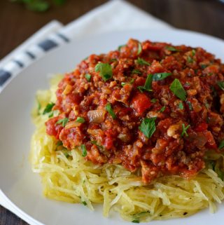A white plate with shredded spaghetti squash topped with Italian meat sauce.