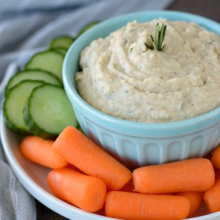 A bowl of white bean hummus on a plate with raw veggies.
