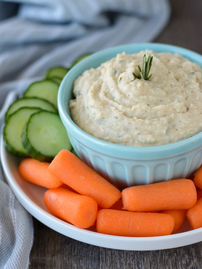 A bowl of white bean hummus on a plate with raw veggies.