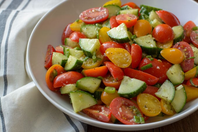A large bowl with Tomato and Cucumber Salad tossed with a Parmesan Garlic Vinaigrette.