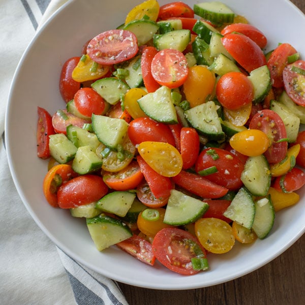 A large bowl with Tomato and Cucumber Salad tossed with a Parmesan Garlic Vinaigrette.