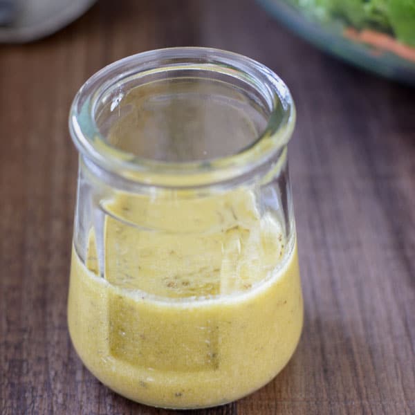 A glass jar with apple cider vinaigrette dressing and a large green salad in the background.