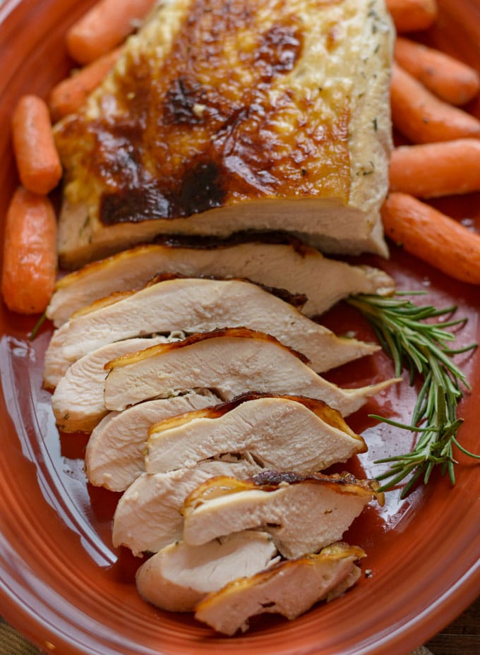 A large platter with sliced turkey breast, carrots and a sprig of rosemary. 