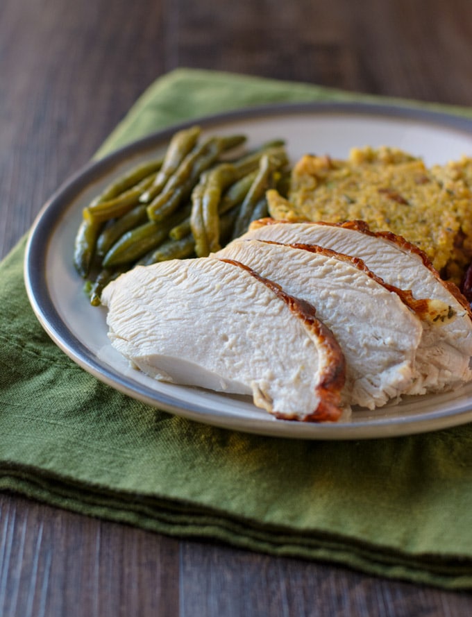A plate with slices of roasted turkey, green beans and cornbread dressing on it. 