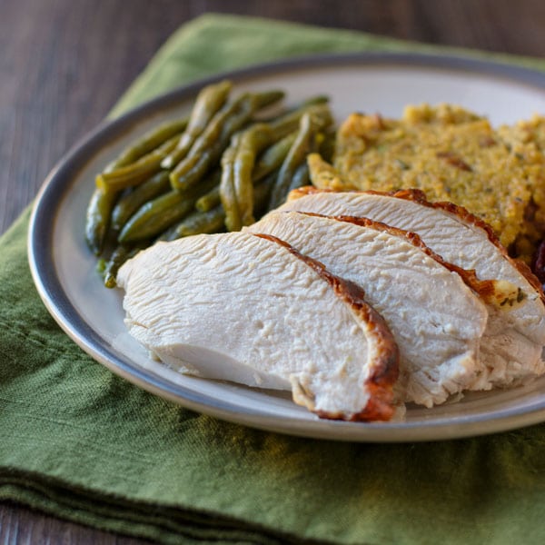 Sliced turkey breast on a plate with cornbread dressing and green beans.